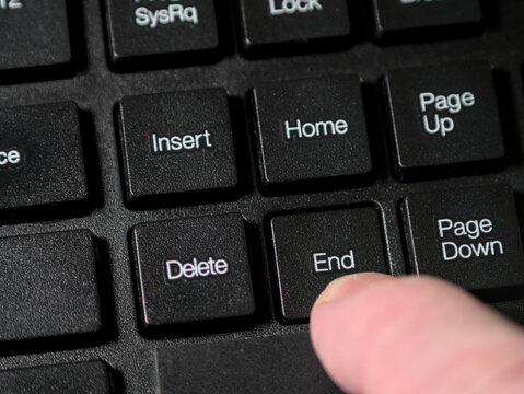 A person's finger pressing the End key on a black computer keyboard. Close up, macro shot