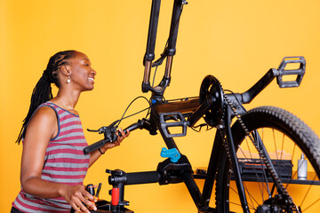 Athletic black woman engrossed in fixing broken bike components with specialist tools. African...