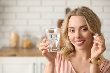 Young woman with glass of water and pills in kitchen, closeup