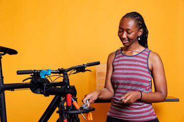 Fototapeta na wymiar Dedicated black woman selects and examines several equipment from a professional toolkit for bike repair. Active african american lady clutching and arranging specialized bicycle maintenance tools.