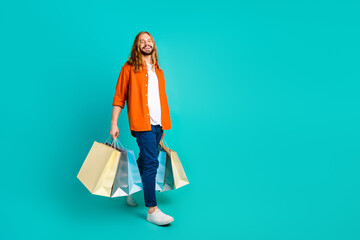 Full length body photo of handsome blond hair funny man in trendy outfit steps shopping mall isolated on aquamarine color background