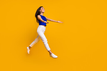 Fototapeta na wymiar Full length photo of pretty excited woman wear blue top jumping holding arms empty space isolated yellow color background
