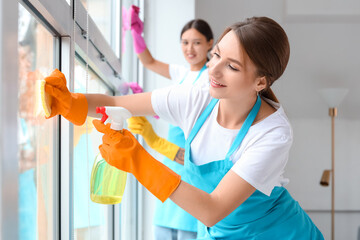 Female janitor cleaning window in room