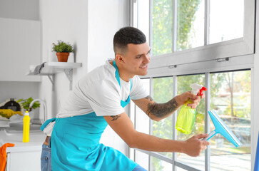 Male janitor cleaning window in kitchen