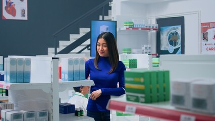 Smiling asian customer amidst pharmacy shelves, looking at medicine packages, trying to find...
