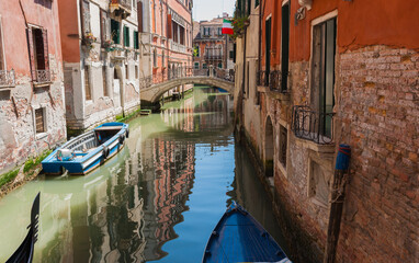 Blue barge moored against brick wall in narrow Venice canal by bridge