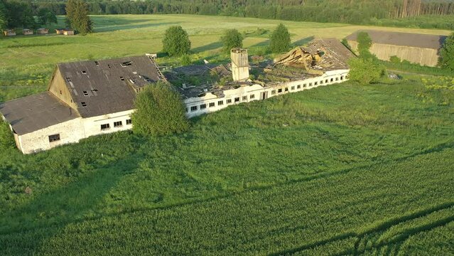 Paide, Estonia-July 5.2021: Aerial shot of an old forgotten soviet farm building. Slowly decaying structure becoming one with nature. Drone moving away from the barn.