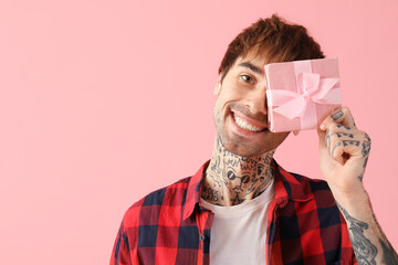 Funny young man with gift for Valentine's day on pink background