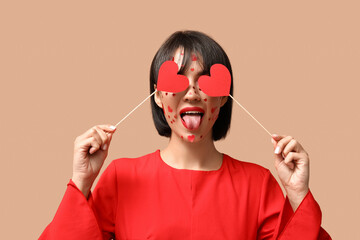 Funny young young woman with creative makeup for Valentines Day and hearts on beige background