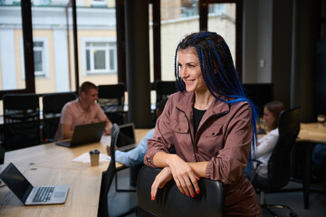 Fototapeta premium Side view positive woman marketer standing near workplace with laptop