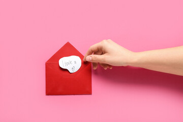 Female hand with red envelope and text I LOVE U on pink background, closeup. Valentine's Day...