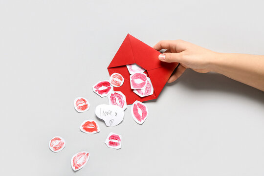 Female hand with red envelope, paper lipstick kiss marks and text I LOVE U on grey background, closeup. Valentine's Day celebration