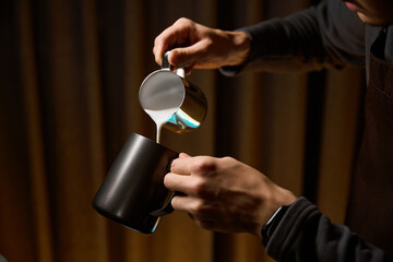 Unrecognizable barista pouring milk from pitcher preparing coffee