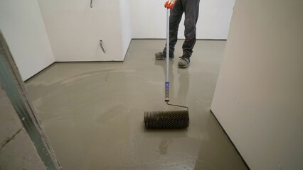 A worker applies epoxy resin to a new floor. Fill the floor, roll out the mixture with a needle roller. Needle roller when pouring the floor. Needle roller for self-leveling floors. 
