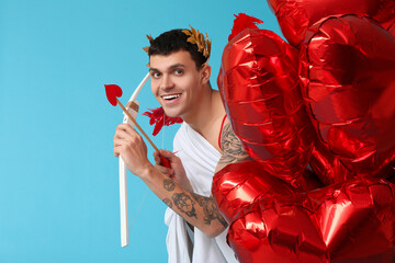 Young man dressed as Cupid with bow and balloons on blue background. Valentine's Day celebration