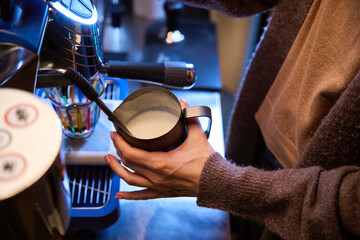 Unknown woman bartender barista whisking milk for latte in steel jug