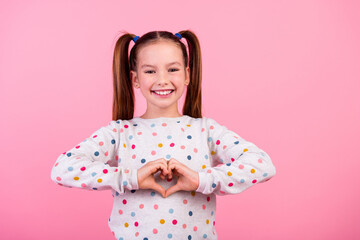 Photo of friendly nice small girl with tails hairstyle wear stylish sweatshirt showing heart symbol isolated on pink color background - obrazy, fototapety, plakaty