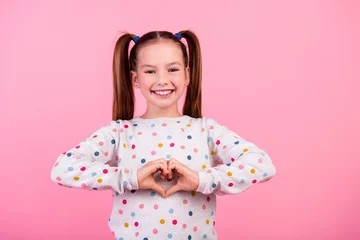 Foto op Canvas Photo of friendly nice small girl with tails hairstyle wear stylish sweatshirt showing heart symbol isolated on pink color background © deagreez