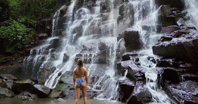 A young woman in a swimming suit at Kanto Lampo waterfall in lush tropical forest, Bali, Indonesia