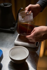 Barista pouring hot aromatic Americano from coffee maker into glass cup