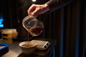 Faceless bartender pouring hot tasty from coffee maker into glass cup