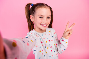 Photo of cheerful small girl with ponytails wear stylish sweatshirt making selfie showing v-sign...