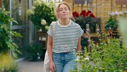 Woman inside greenhouse in garden centre choosing and buying red Echinacea plant - shot in slow motion