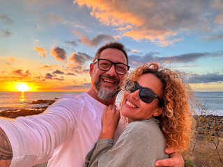 Happy adult couple in love taking selfie picture with romantic wonderful sunset on the ocean in...