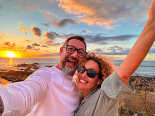 Crazy happy couple of tourist taking selfie picture at the beach with amazing sunset in background....