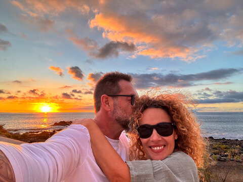 Romantic couple of man and woman in love taking selfie picture together hugging and smiling at the phone camera and enjoying beautiful sunset on the ocean at the beach. Travel people summer vacation