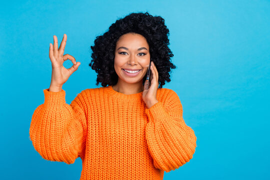 Photo portrait of young woman talk phone show okey symbol dressed stylish knitted orange clothes isolated on blue color background