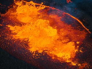 Dramatic view of dark volcanic landscape with glowing melting lava boiling in the crater, active volcano during eruption in Iceland, aerial shot.