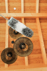 fluffy bristle brush cleans metal black lamps under a wooden ceiling.Dust cleaning. Bottom view....