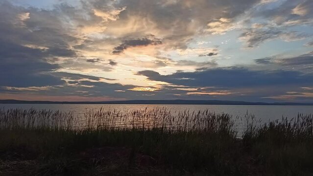 The setting sun turns clouds over a large lake orange on a summer evening. Lake Bele, Khakassia, Siberia, Russia.