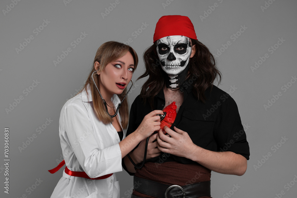 Poster couple in scary nurse and pirate costumes with heart model and stethoscope on light grey background.