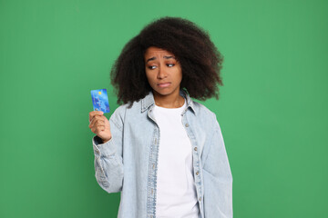 Confused woman with credit card on green background. Debt problem
