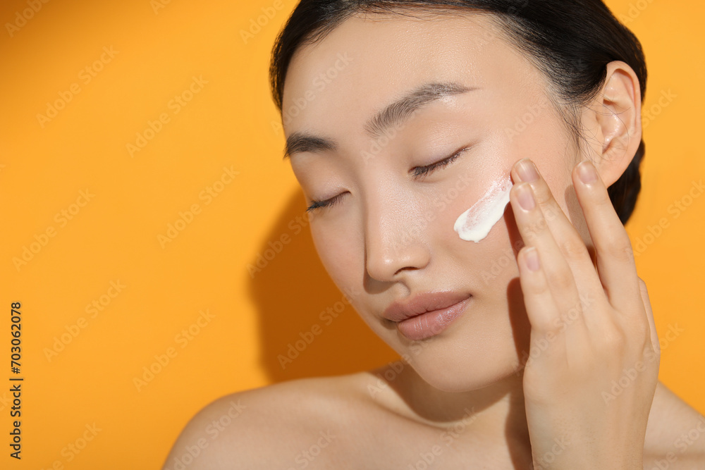 Canvas Prints Beautiful young woman in sunlight with sun protection cream on her face against orange background, closeup. Space for text