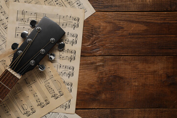Paper sheets with music notes and acoustic guitar on wooden table, top view. Space for text