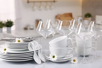 Set of clean dishware, glasses, cutlery and flowers on table in kitchen