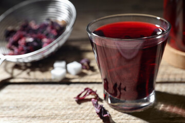 Delicious hibiscus tea in glass on wooden table, closeup. Space for text