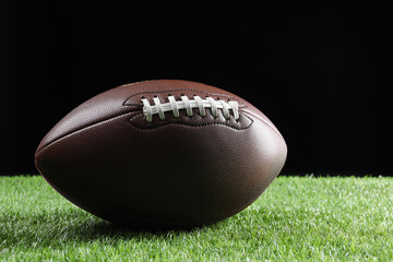 Leather American football ball on green grass against black background