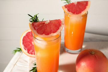 Tasty grapefruit drink with ice in glasses, rosemary and fresh fruits on light table, closeup