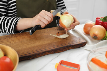 Woman peeling fresh onion with knife at white marble table indoors, closeup