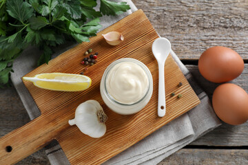 Fresh mayonnaise sauce in glass jar and ingredients on wooden table, flat lay