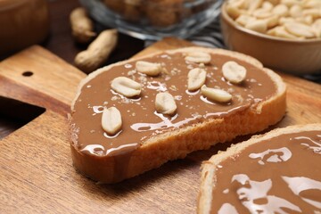 Toasts with tasty nut butter and peanuts on wooden board, closeup