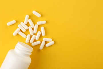 Bottle and vitamin capsules on yellow background, top view. Space for text