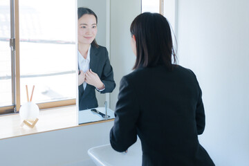 洗面所の鏡を見る若いビジネスウーマン（美容）
