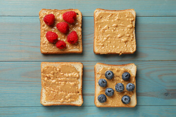 Delicious toasts with peanut butter, raspberries and blueberries on light blue wooden table, flat lay