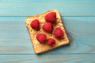 Delicious toast with peanut butter and raspberries on light blue wooden table, top view