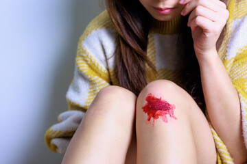 膝を擦りむいて床に座る女性（顔なし）